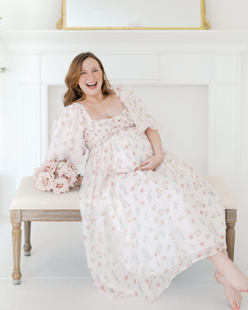 girl wearing pink and white floral dress holds her pregnant belly in a minneapolis studio for her minneapolis maternity photography session.