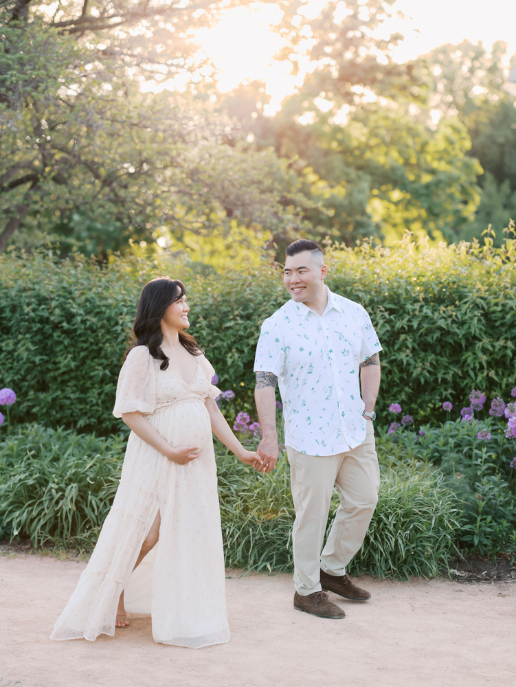 husband and wife walk hand in hand at lyndale park rose garden for their minneapolis maternity photoshoot