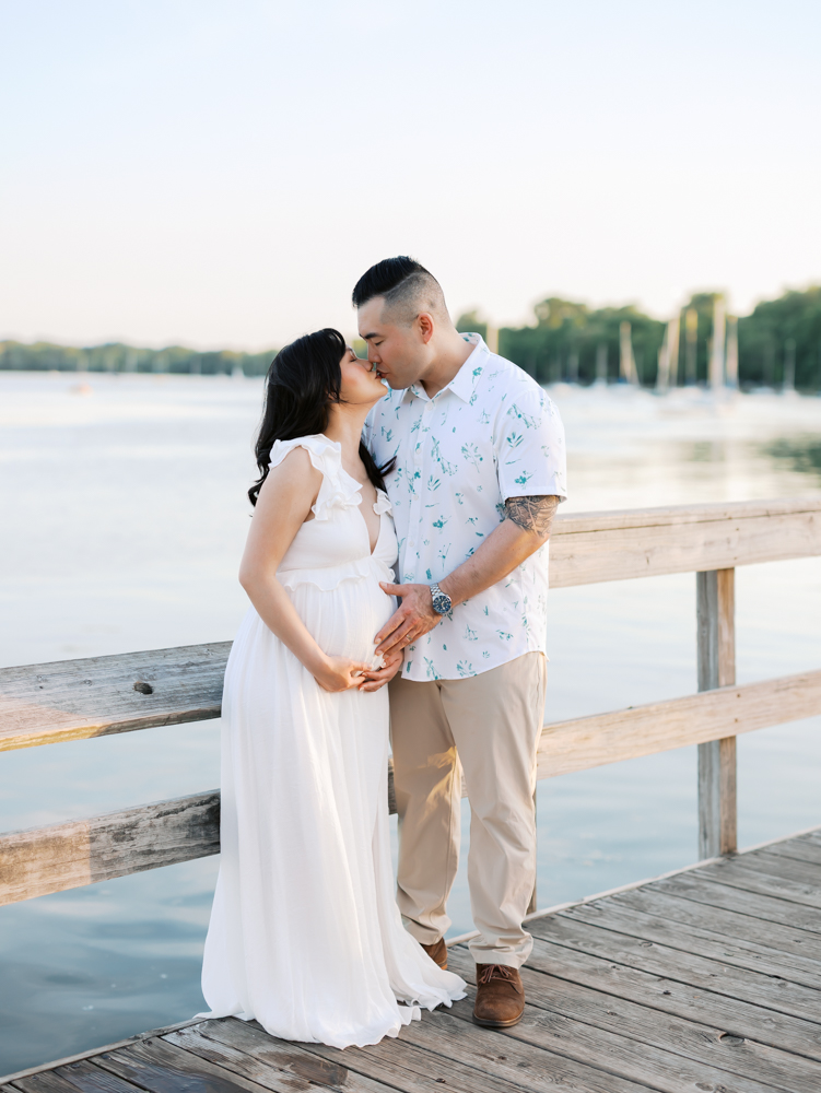 husband and wife share a kiss on the pier at lake harriet for their minneapolis maternity photoshoot