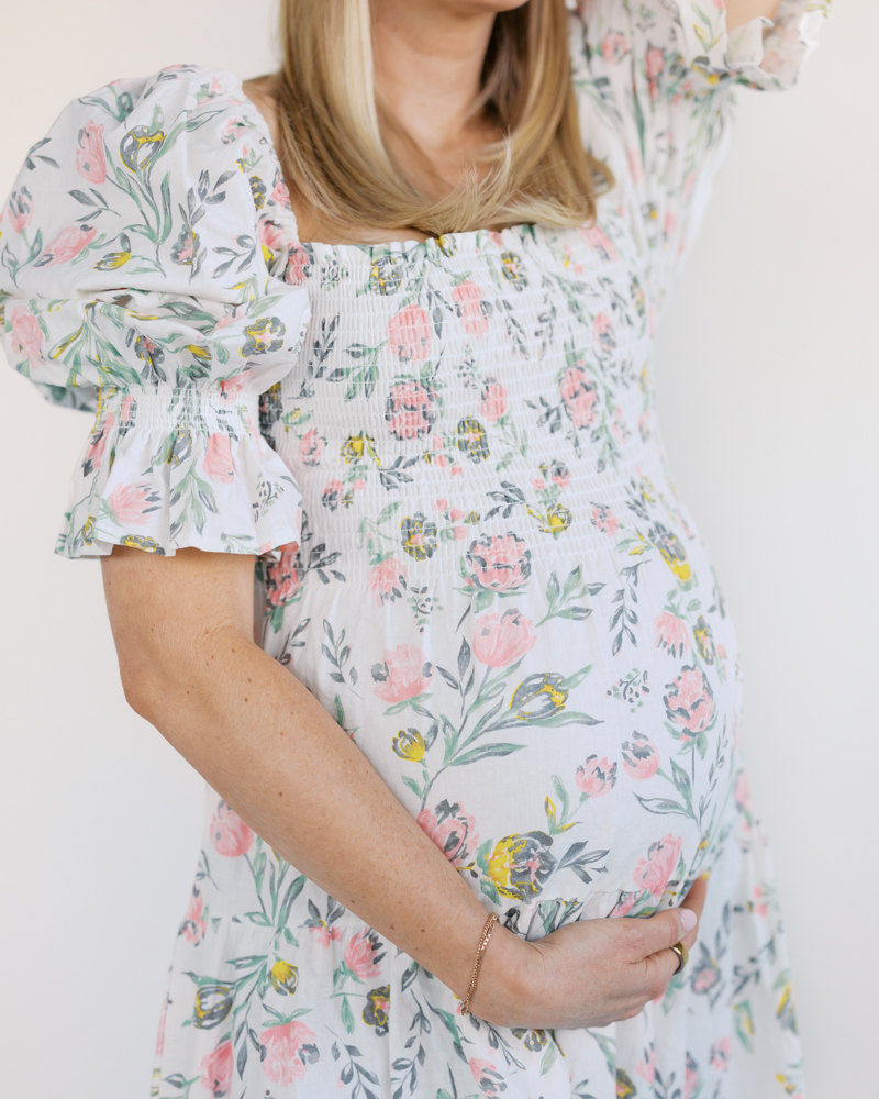 Woman in pink and white floral dress holds her pregnant belly during her miinneapolis maternity photography session.