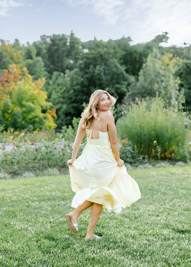 girl in long yellow dress runs in the gardens near the wayzata library for her minneapolis senior pictures