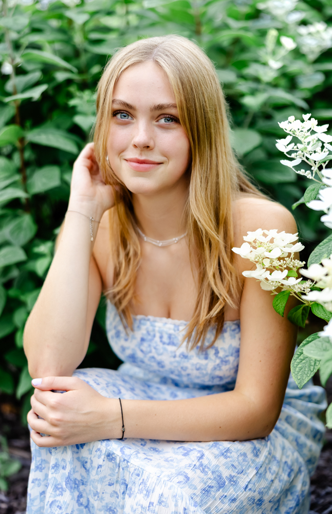 girl in blue and white dress poses by beautiful hydrangeas for her minneapolis senior photos