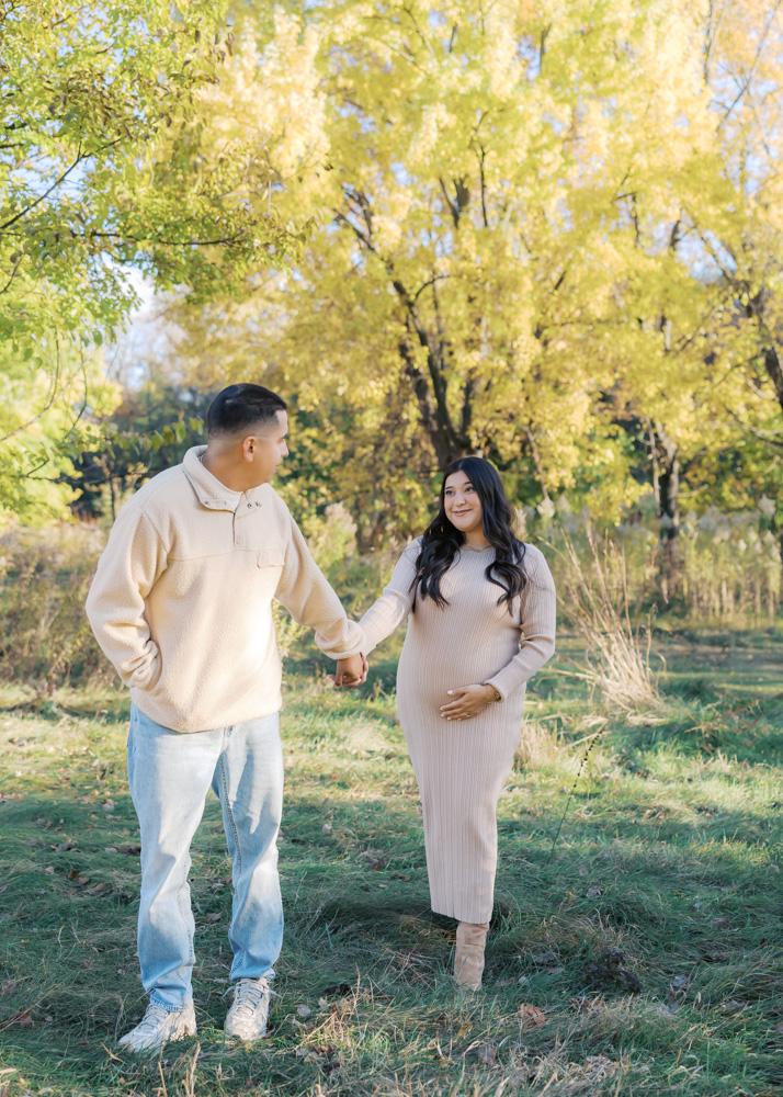 husband and wife hold hands at longfellow gardens in minneapolis for their maternity photography session