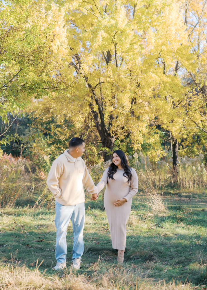 husband and wife hold hands at longfellow gardens in minneapolis for their maternity photography session