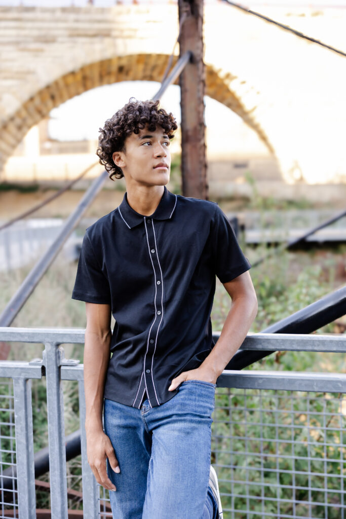 boy in black shirt and jeans poses at mill ruins park for his minneapolis senior pictures