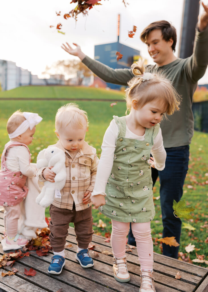 dad throws leaves in the air at his 3 young kids at gold medal park for their minneapolis family photos