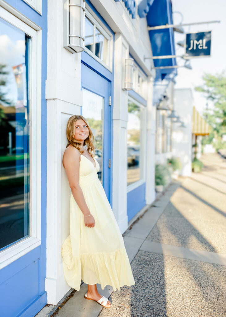 girl in yellow dress poses in front of downtown wayzata store fronts for her minneapolis senior pictures photography session