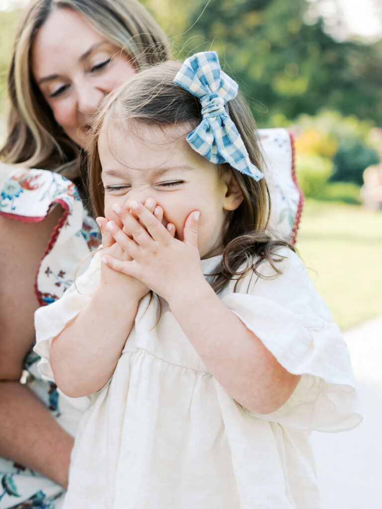 young girl laughts and covers her mouth during her family photography session at arneson acres park, minnesota