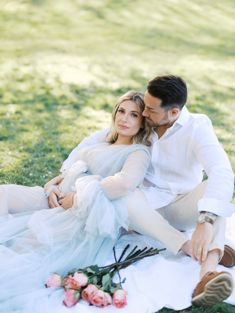 husband and wife sit on a white blanket next to pink long stemmed roses during their minneapolis maternity photography session