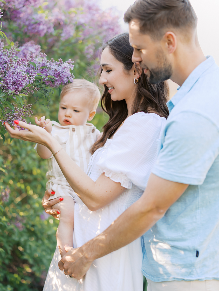 mom, dad and 14 month old smell the lilacs at lyndale park gardens for their minneapolis family photography session